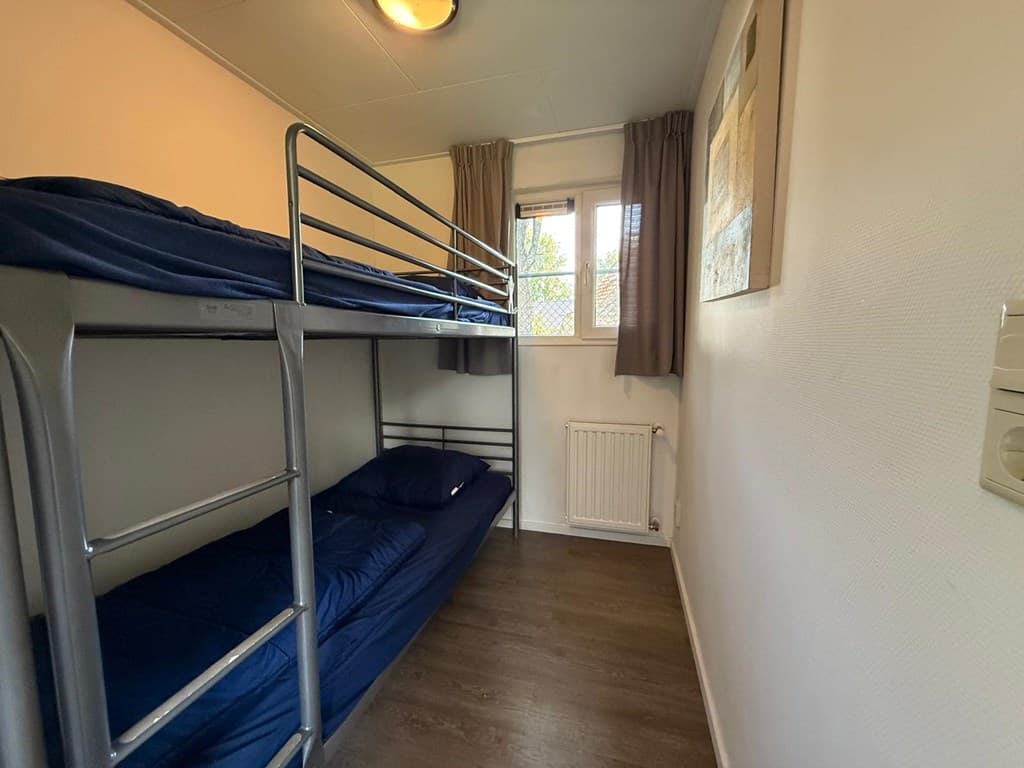 Slaapkamer met stapelbed en raam, neutrale kleuren en houten vloer.