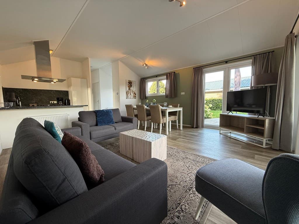 Woonkamer met moderne meubels, eettafel en toegang tot een tuin via glazen schuifdeur