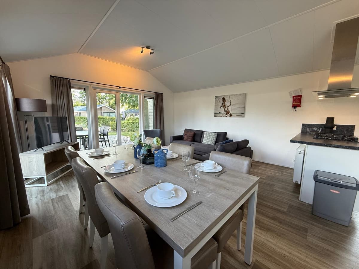 Woonkamer met eettafel, bank en moderne keuken in een vakantiewoning met uitzicht op buitenveranda.