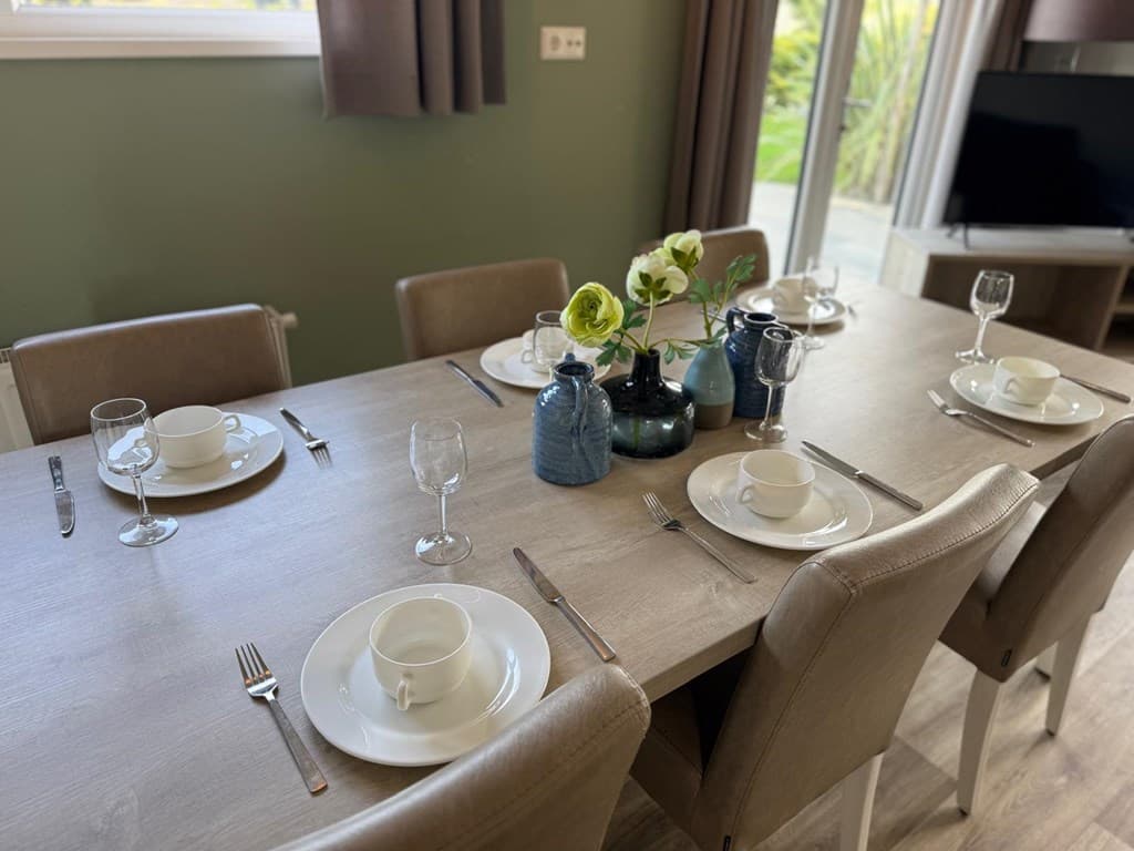 Dining table met zes borden, glazen en bestek, versierd met vazen en bloemen, met uitzicht op de tuin.