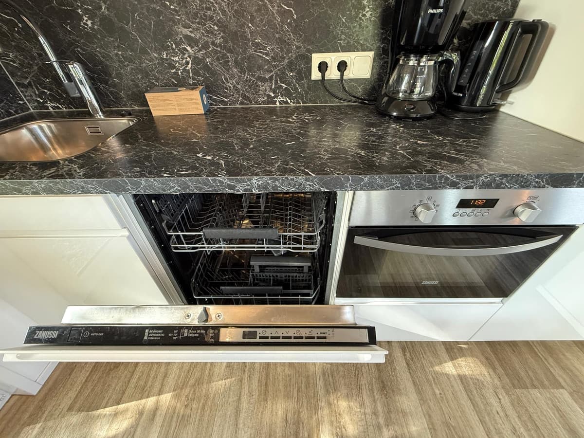 Keuken met zwart marmeren werkblad, spoelbak, vaatwasser en oven, koffiezetapparaat zichtbaar naast elkaar.