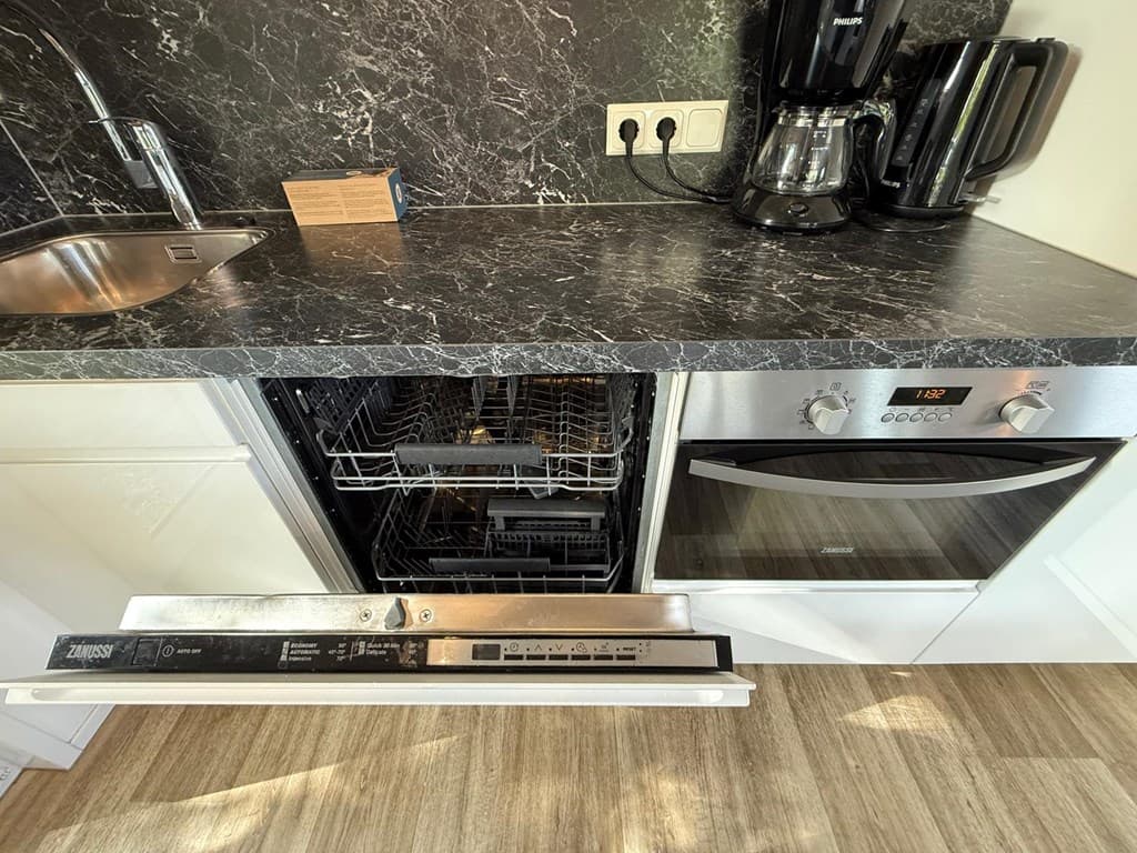 Keuken met zwart marmeren werkblad, spoelbak, vaatwasser en oven, koffiezetapparaat zichtbaar naast elkaar.