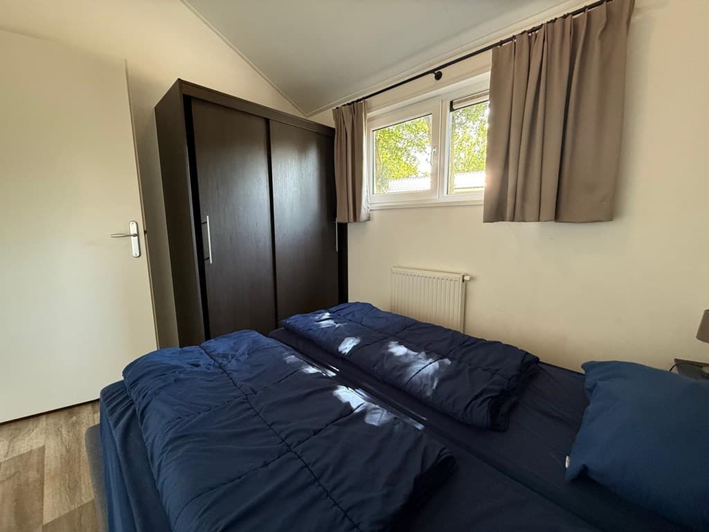 Slaapkamer met twee eenpersoonsbedden, kledingkast en een klein raam met gordijnen.