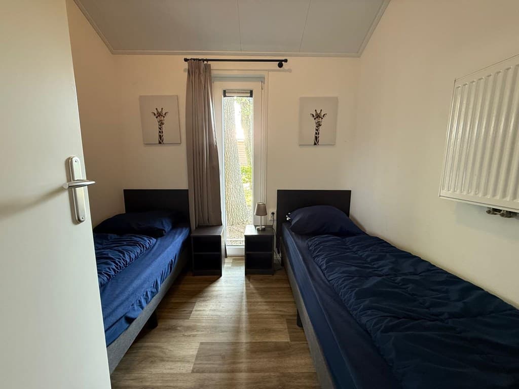 Slaapkamer met twee eenpersoonsbedden, nachtkastjes en toegang tot een veranda met uitzicht op de tuin.