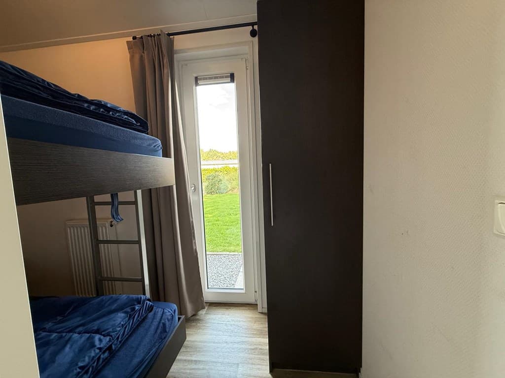 Slaapkamer met stapelbed, kast, raam met uitzicht op buitenruimte en toegang tot het terras.