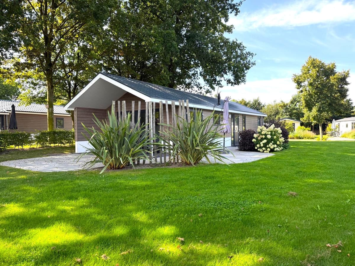 Vakantiewoning met een groene tuin, moderne gevel en houten elementen, omgeven door bomen en struiken.