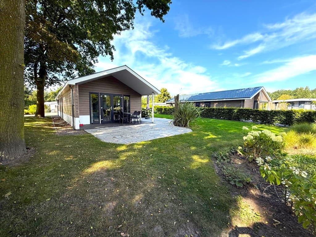 Vakantiewoning met ruime patio, groene tuin en uitzicht op omliggende woningen en bomen.