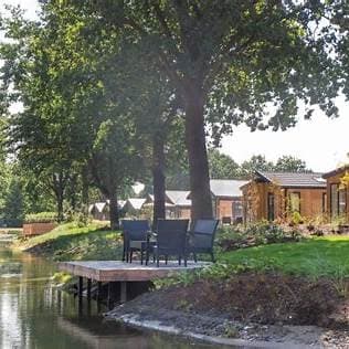 Terras met stoelen aan het water en uitzicht op vakantiehuisjes omringd door bomen en groen.