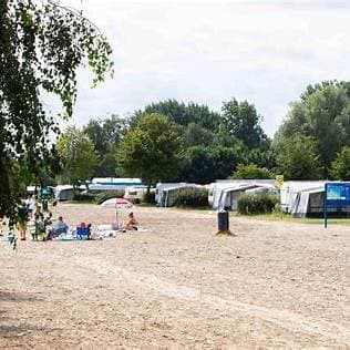 Zicht op een rustige camping met huurtenten, bomen en een zandpad tussen de percelen in EuroParcs Zuiderzee.