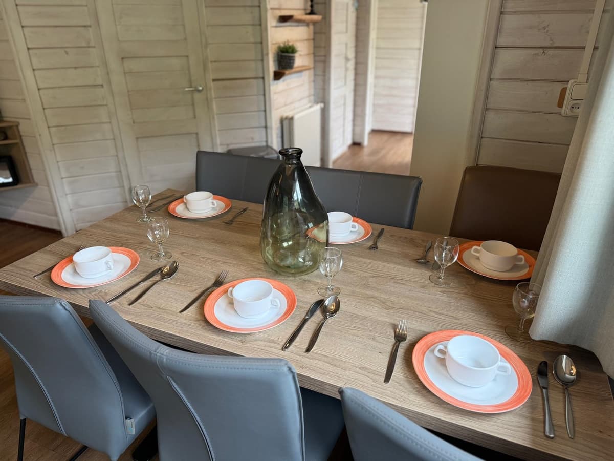 Eettafel met zes plaatsen, gedekt met servies en glazen in een moderne woonkamer met houten wanden.