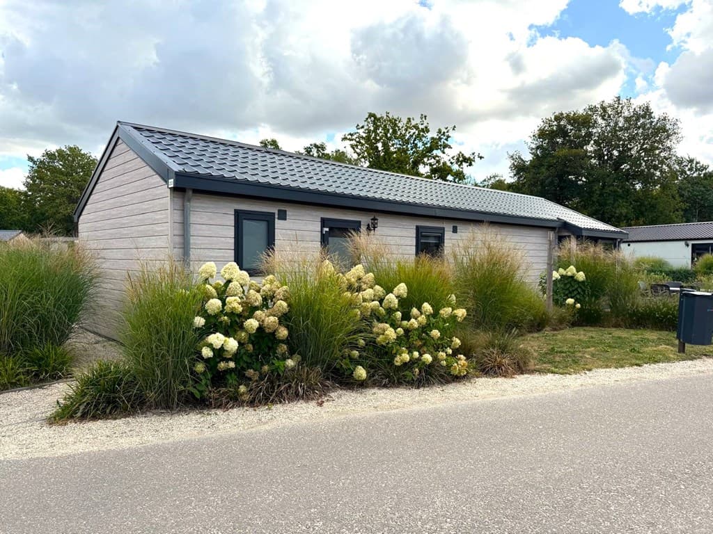 Moderne vakantiewoning met een lichte houten gevel, omringd door groene siergrassen en bloeiende hortensia's