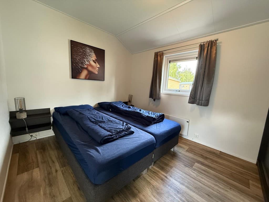 Slaapkamer met twee eenpersoonsbedden, een raam met gordijnen en een kunstwerk aan de muur
