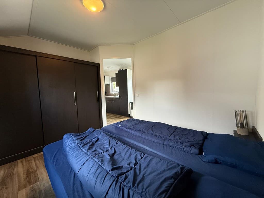 Slaapkamer met een bed met blauwe dekens, grote kast en open doorgang naar een andere ruimte.