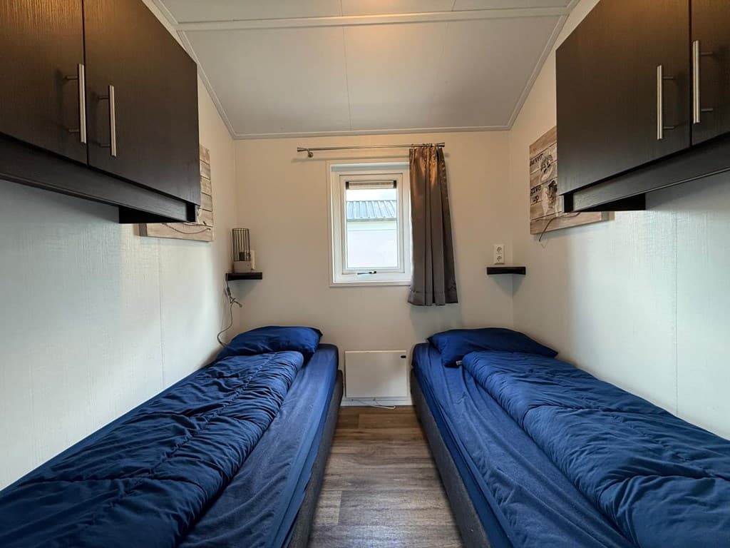 Slaapkamer met twee enkele bedden en wandkasten, raam met gordijnen zichtbaar