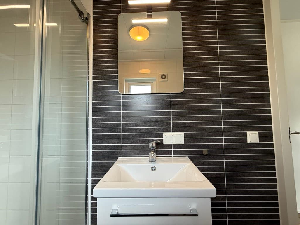 Moderne badkamer met een wastafel, spiegel en douchewand met zwarte tegels op de wand.
