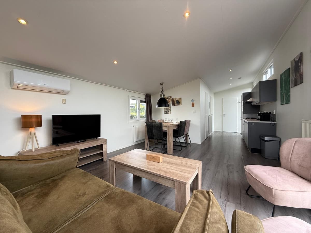 Lichte woonkamer met zithoek, eettafel en open keuken, grote ramen zorgen voor veel natuurlijk licht