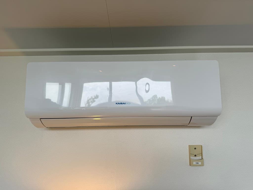 Witte wandairconditioning gemonteerd boven een wand met een lichte textuur