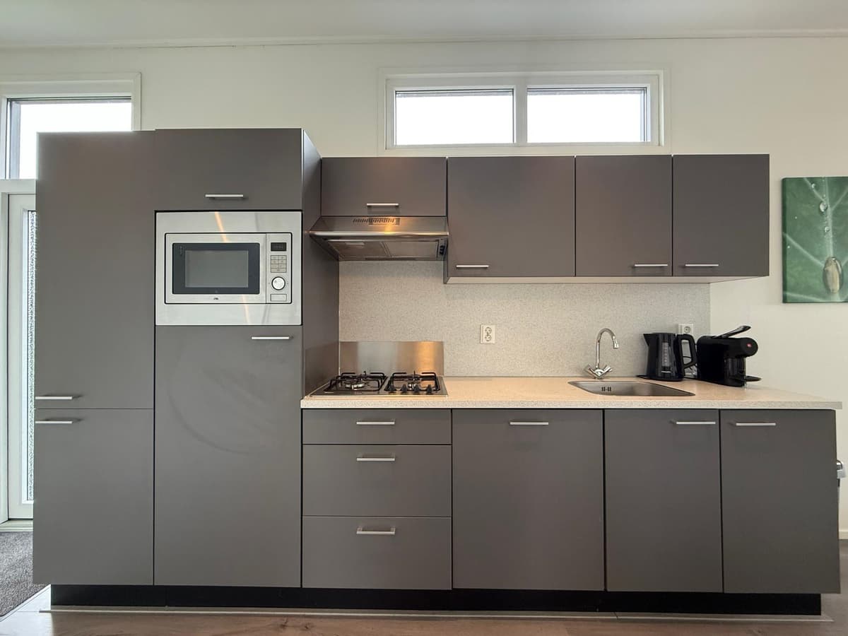Moderne keuken met grijze kasten, een magnetron, gasfornuis en een kleine spoelbak.