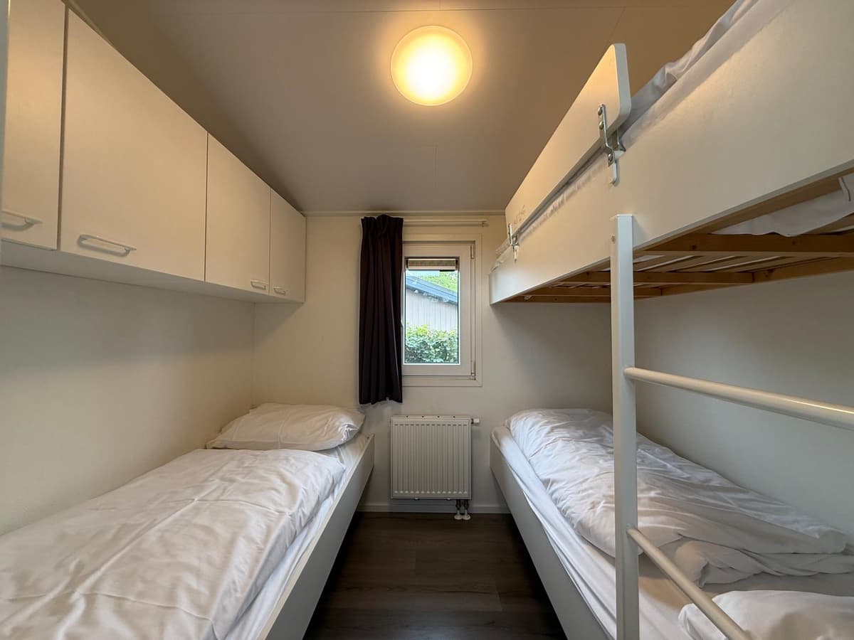 Slaapkamer met twee eenpersoonsbedden, een stapelbed en kastjes boven de bedden, raam met zicht naar buiten.