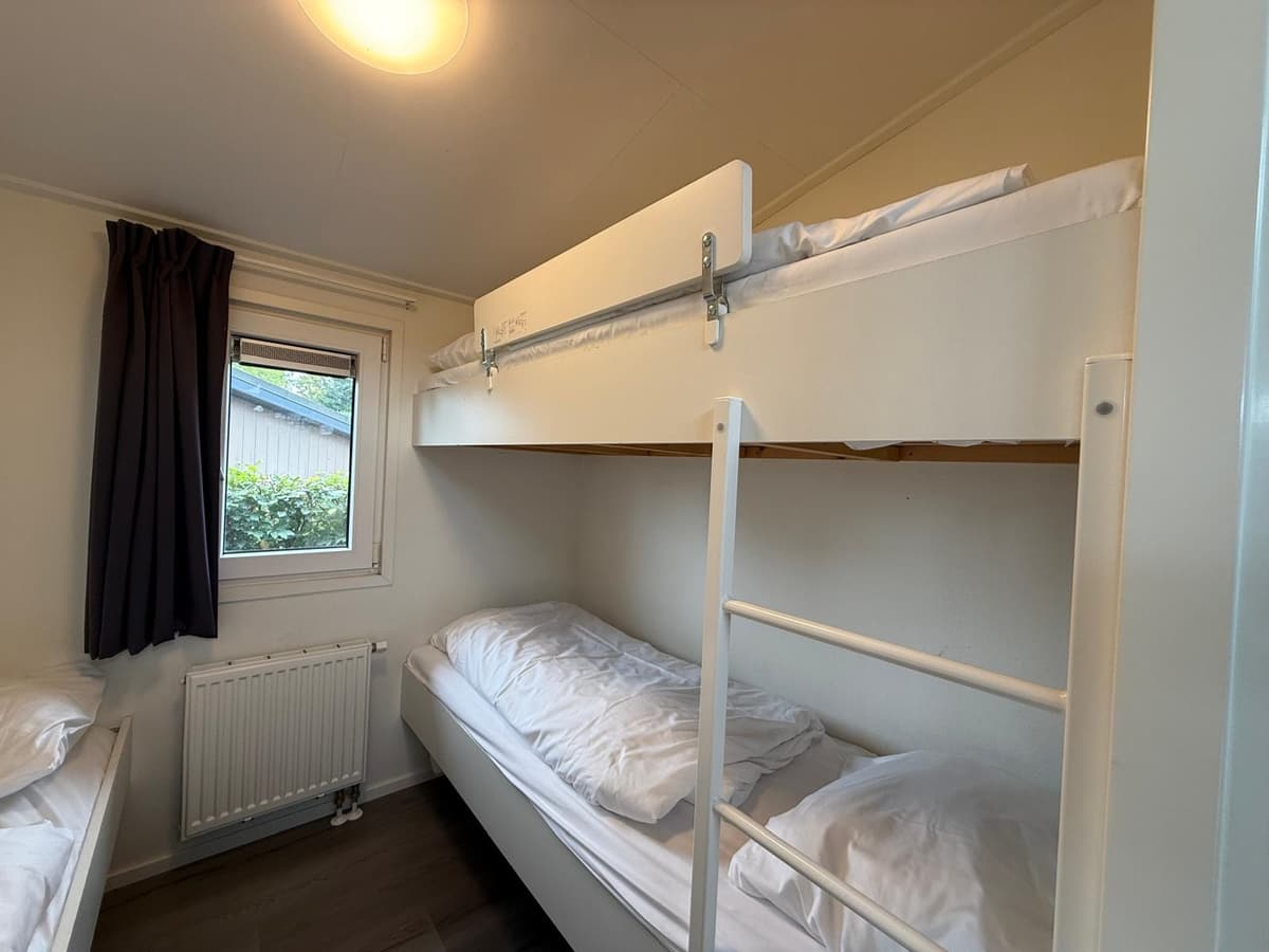 Slaapkamer met stapelbed en een bed, raam met gordijnen en radiator zichtbaar