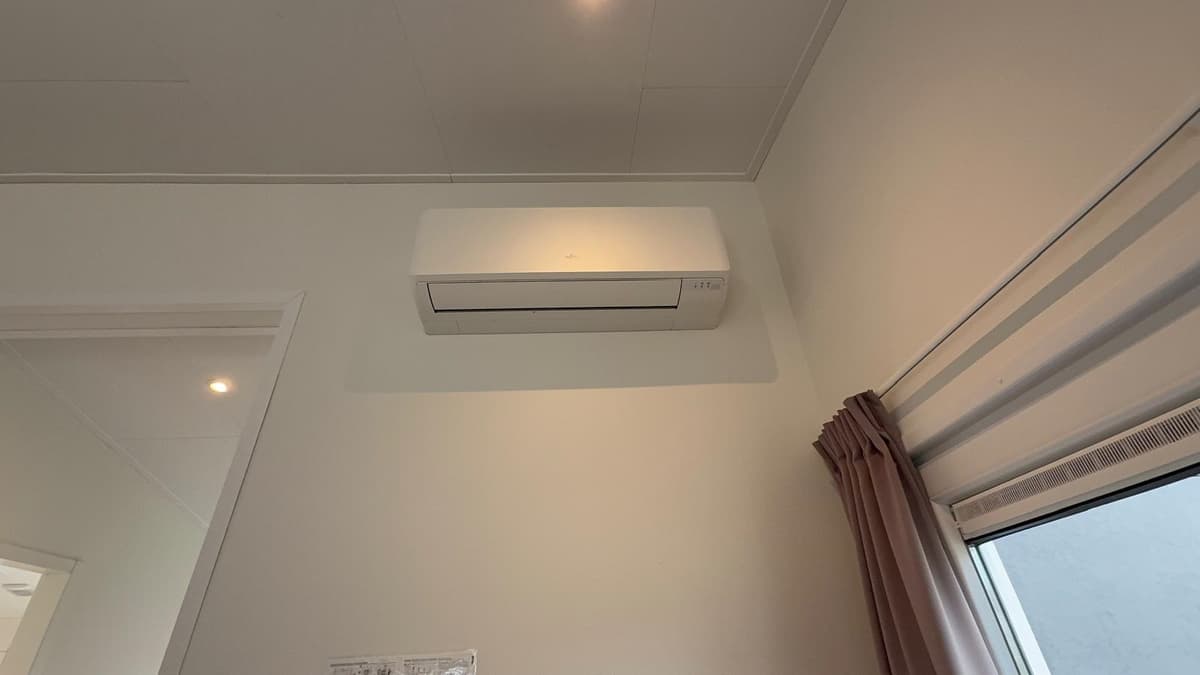 Wandairconditioner boven een raam met gordijnen in een lichte kamer