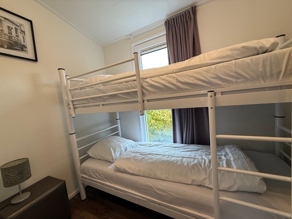 Slaapkamer met stapelbed en een eenpersoonsbed, raam met uitzicht op groen en gordijnen aan de zijkant.