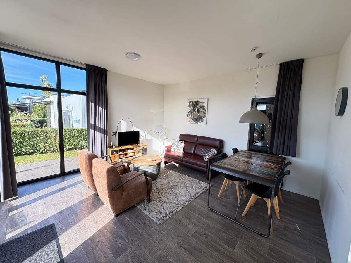 Moderne woonkamer met zithoek, eettafel en grote ramen met zicht op buitenruimte en groen.
