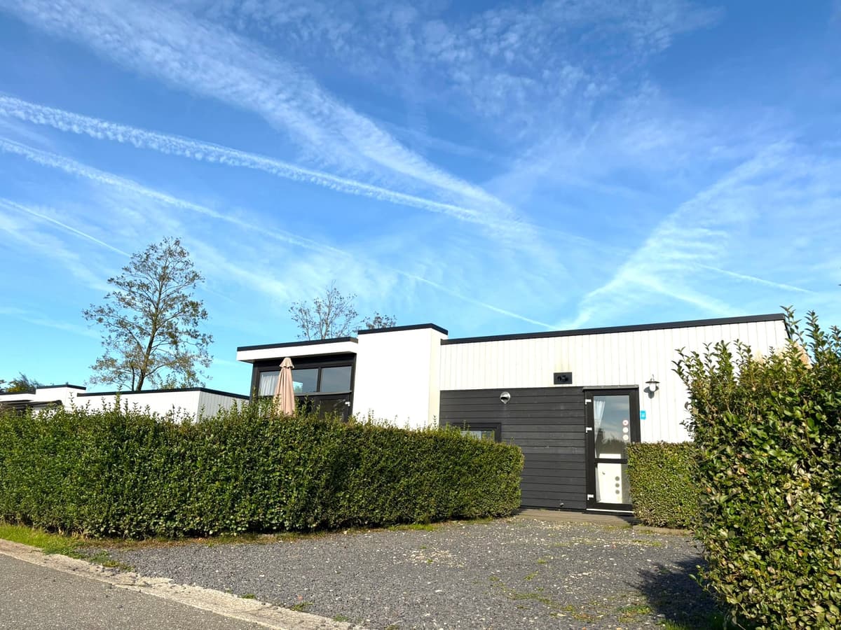 Vakantiehuis met zwarte en witte gevels, omringd door groene heggen en een blauwe lucht met wisbelden.