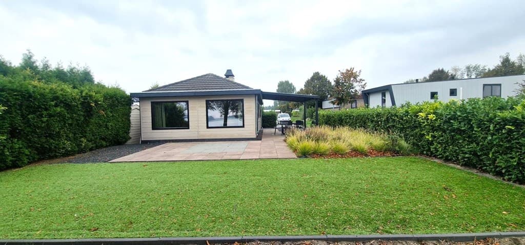 Aanzicht van vakantiehuis met terras, omgeven door groen en een gazon, bij EuroParcs De Biesbosch in Dordrecht