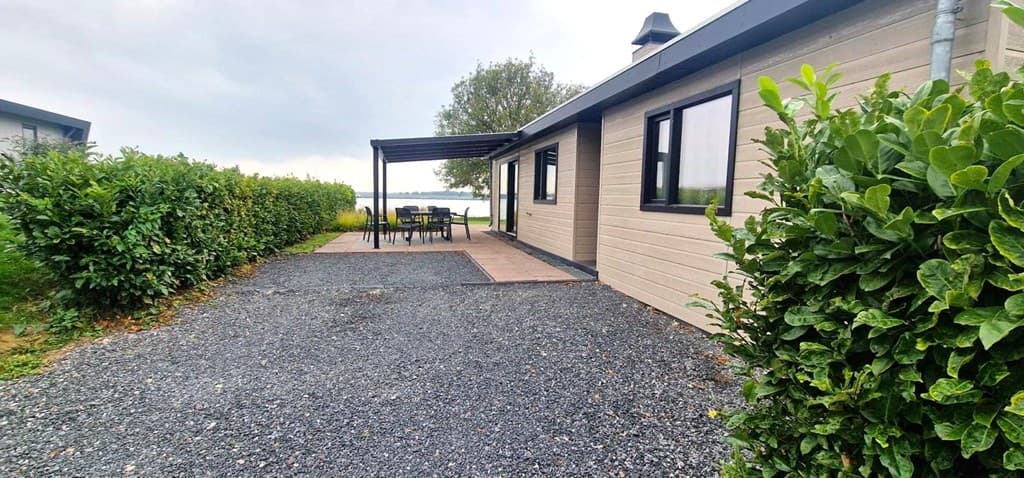 Tuin met grindpad, terras en zithoek, omringd door heggen en met uitzicht op water bij EuroParcs De Biesbosch.