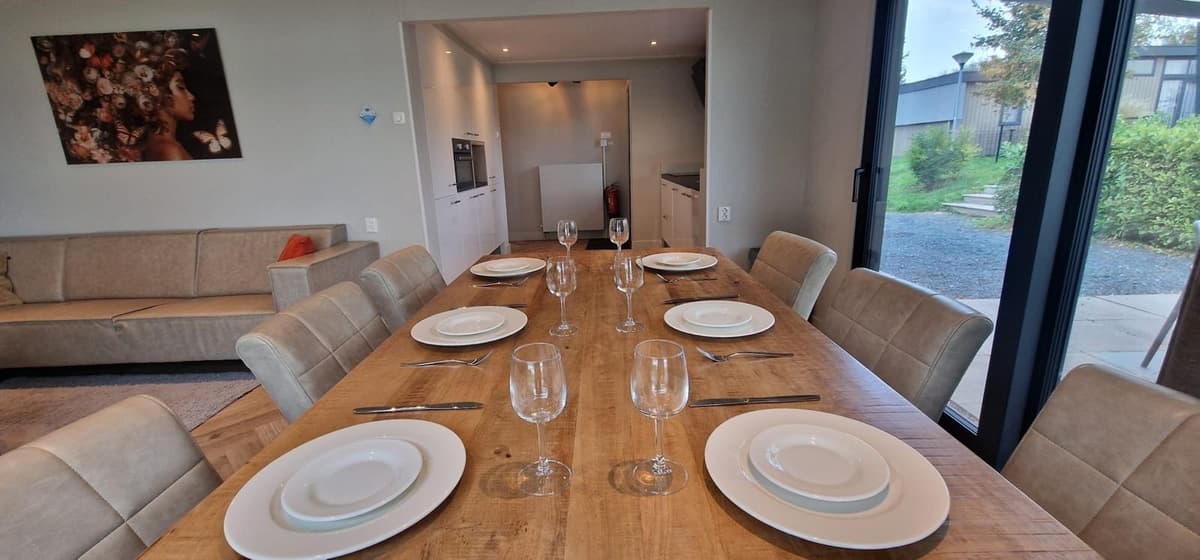 Eettafel met borden en glazen, uitzicht op open keuken en woonkamer met bank en kunst aan de muur.