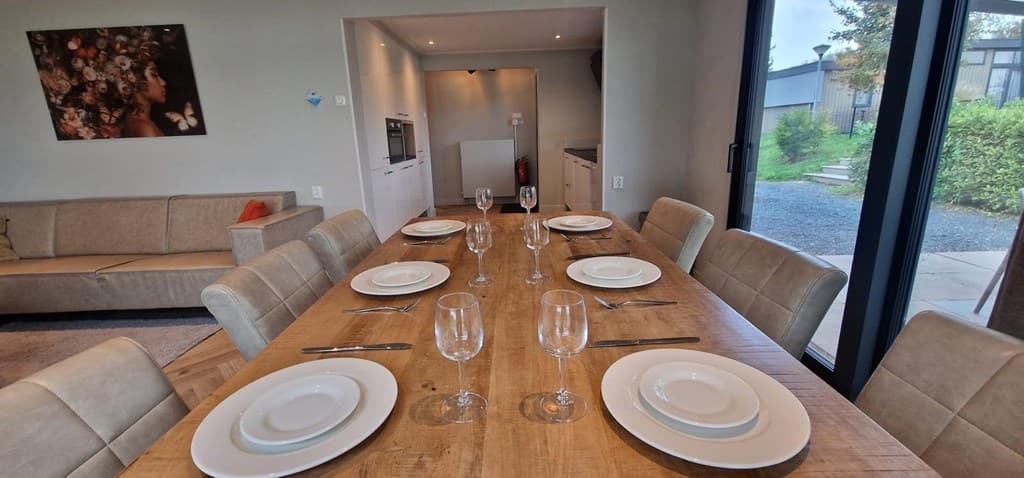 Eettafel met borden en glazen, uitzicht op open keuken en woonkamer met bank en kunst aan de muur.