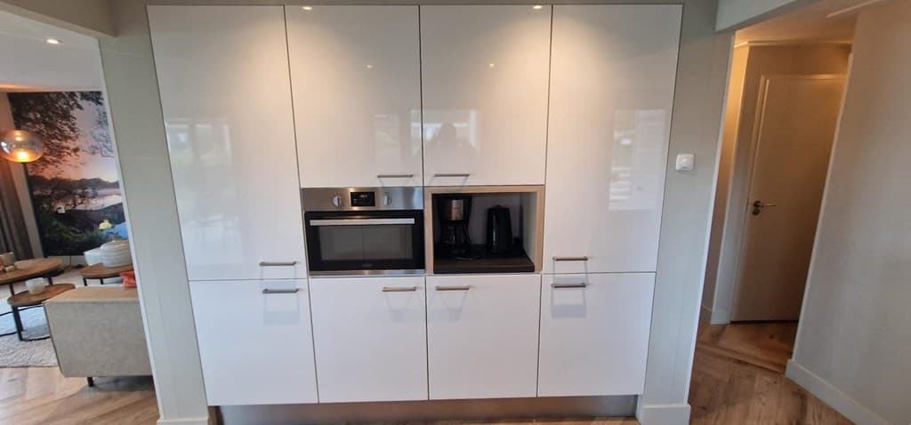 Moderne keukenwand met inbouwapparatuur zoals oven, magnetron en koffiezetter, omgeven door strakke, witte kasten