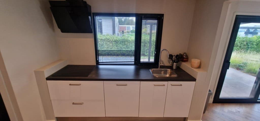 Moderne keuken met een wastafel, een raam met jaloezieën en een strakke werkblad in neutrale kleuren