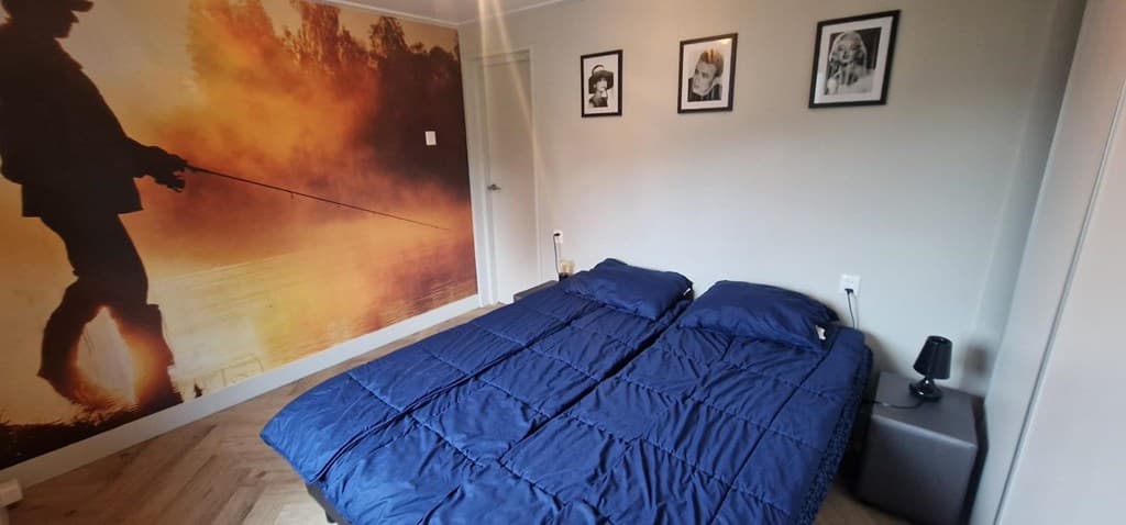 Slaapkamer met twee losse bedden, een opvallende wand met visser-afbeelding en vier fotolijsten aan de muur