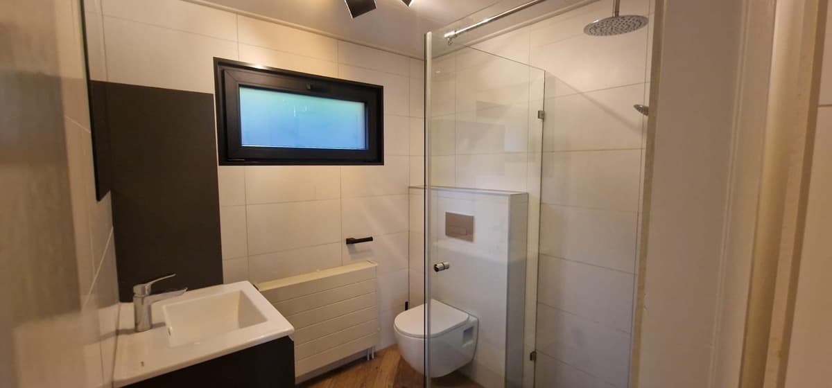 Moderne badkamer met douche, toilet en wastafel in lichte kleurstelling en een klein raam.