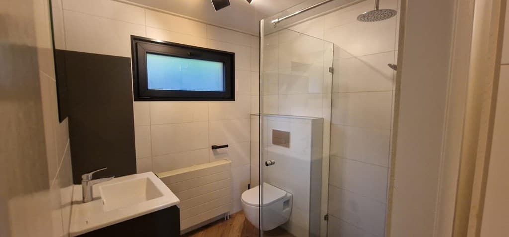 Moderne badkamer met douche, toilet en wastafel in lichte kleurstelling en een klein raam.