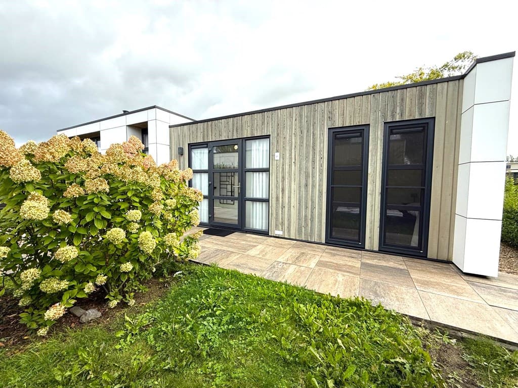 Moderne vakantiewoning met houten gevel en grote ramen, omgeven door een groene tuin en bloeiende hortensia's