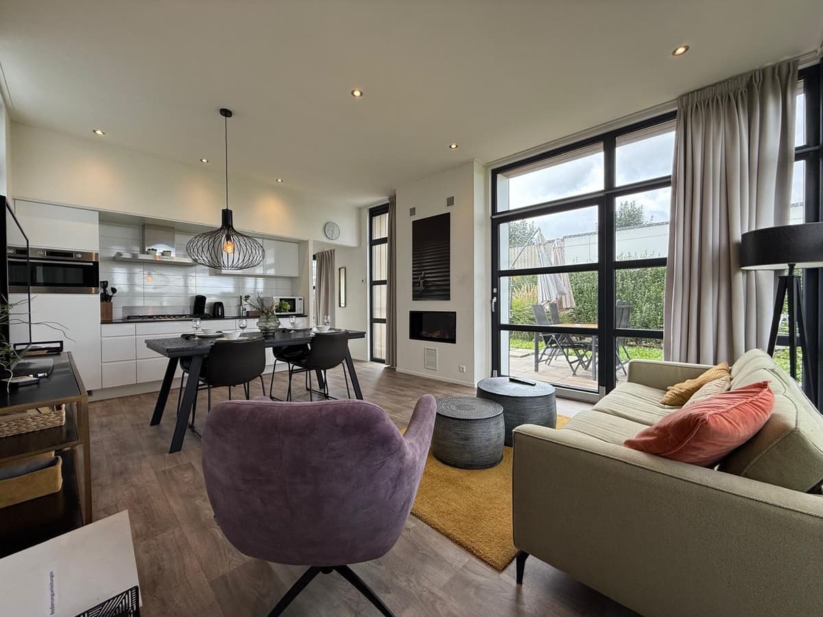 Moderne woonkamer met open keuken, eettafel, luxe bank en grote ramen met uitzicht op het terras.