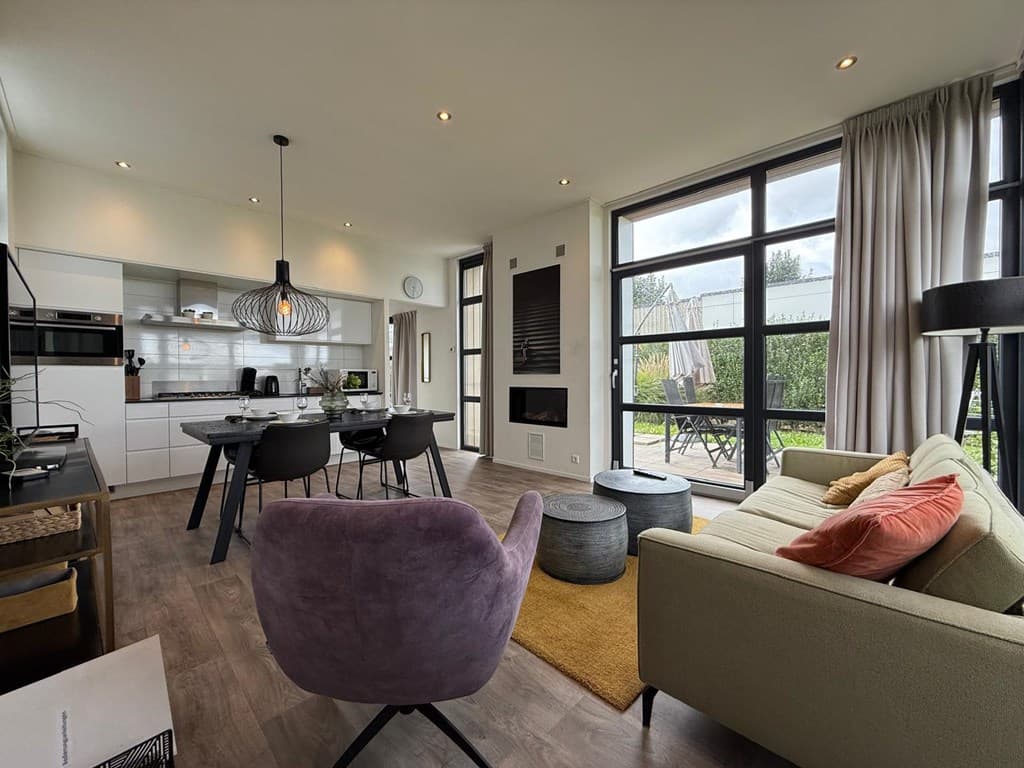 Moderne woonkamer met open keuken, eettafel, luxe bank en grote ramen met uitzicht op het terras.