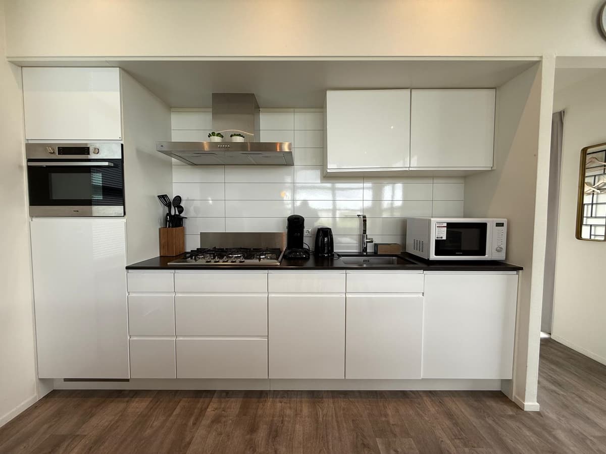 Moderne keuken met witte kasten, ingebouwde oven, kookplaat, magnetron en koffiezetapparaat op een houten vloer