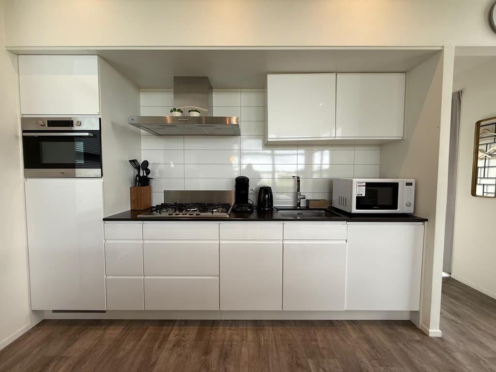 Moderne keuken met witte kasten, ingebouwde oven, kookplaat, magnetron en koffiezetapparaat op een houten vloer