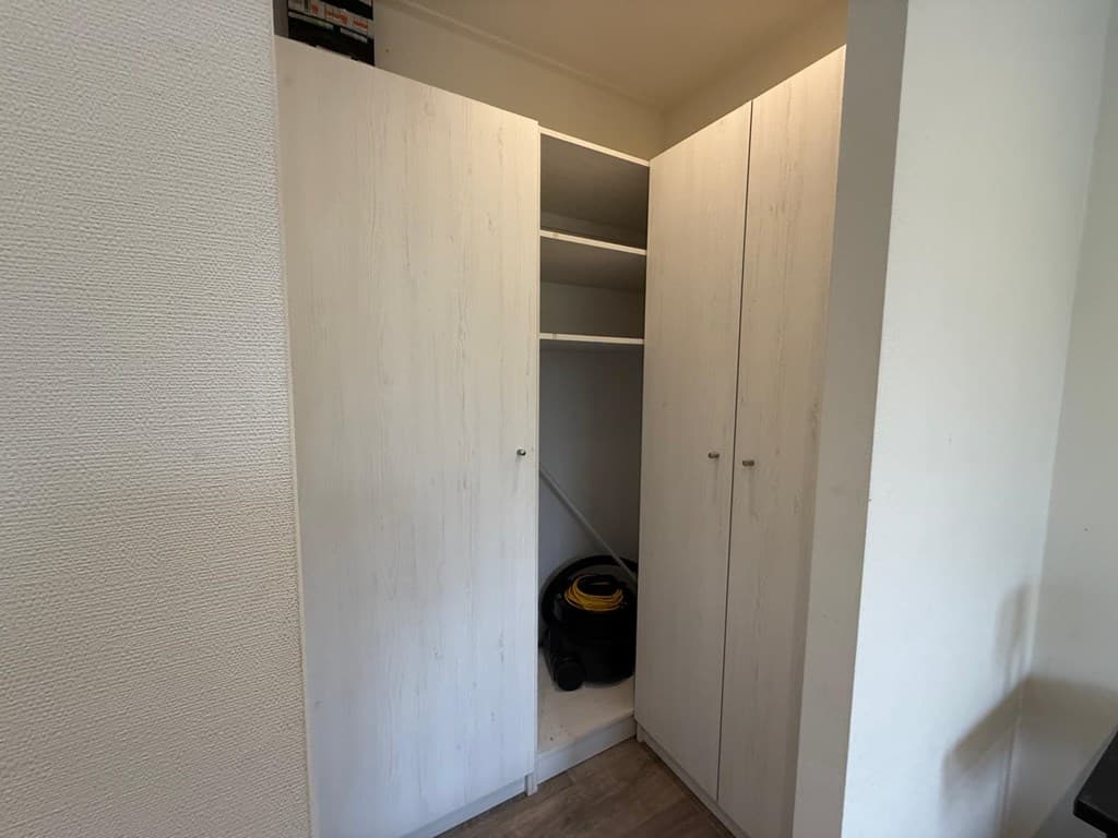 Inbouwkast met planken en een stofzuiger zichtbaar in een lichte ruimte