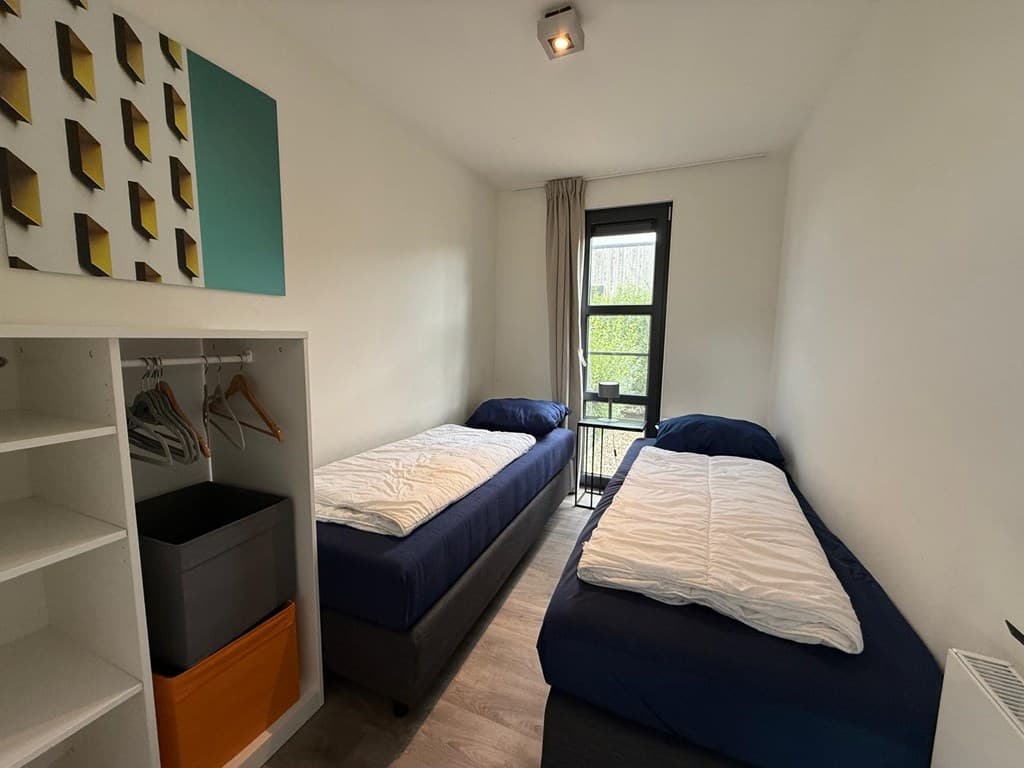 Slaapkamer met twee eenpersoonsbedden, grote ramen en een kast met hangers en opbergbakken.