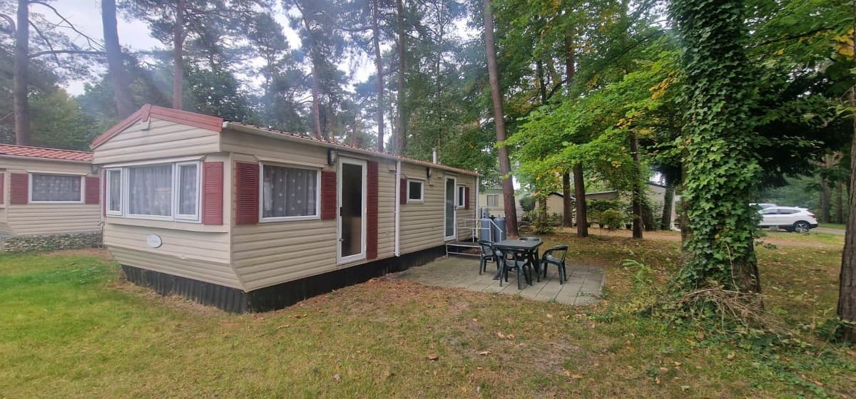 Vrijstaande vakantiewoning met een terras en tuinmeubilair, omringd door bomen en gras.