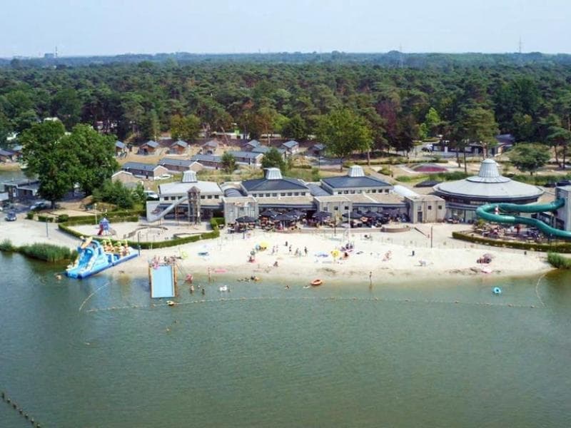 Zicht op het strand en water bij EuroParcs Zilverstrand met gebouw en vakantiehuisjes op de achtergrond.