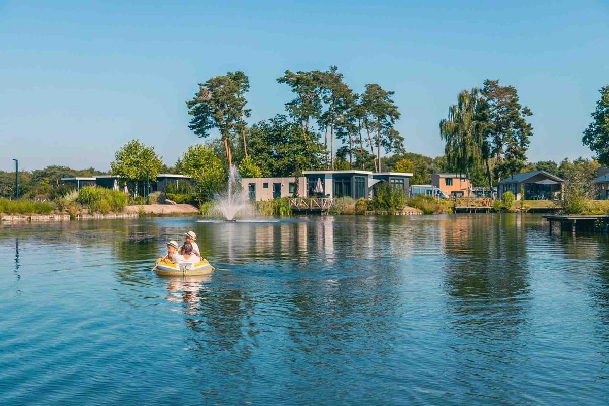 Twee mensen op een bootje varen op een meer omringd door groene bomen en vakantiehuizen in EuroParcs Zilverstrand.
