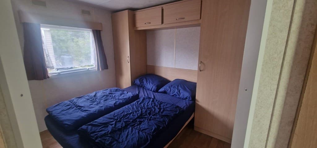 Slaapkamer met twee losse bedden, kasten boven en een raam met gordijnen zichtbaar.