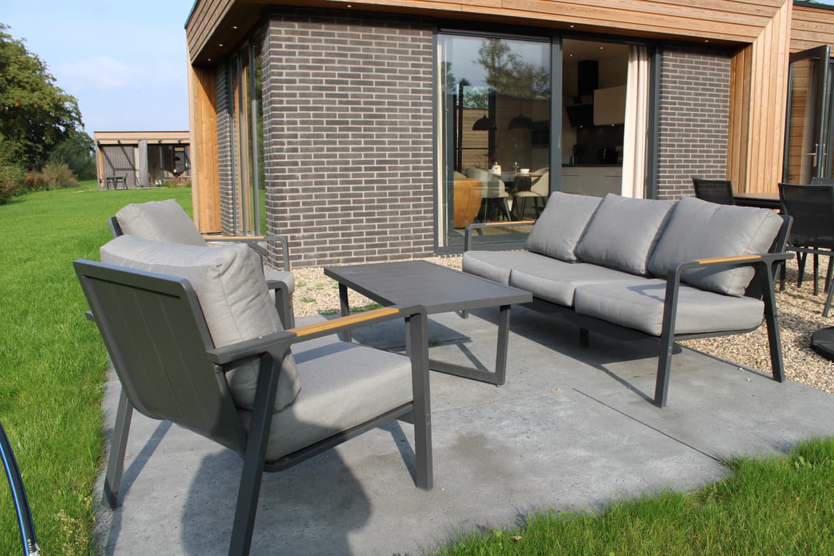 Tuin terras met een zithoek van grijze tuinstoelen en een lage tafel, gelegen op een betegelde ondergrond.