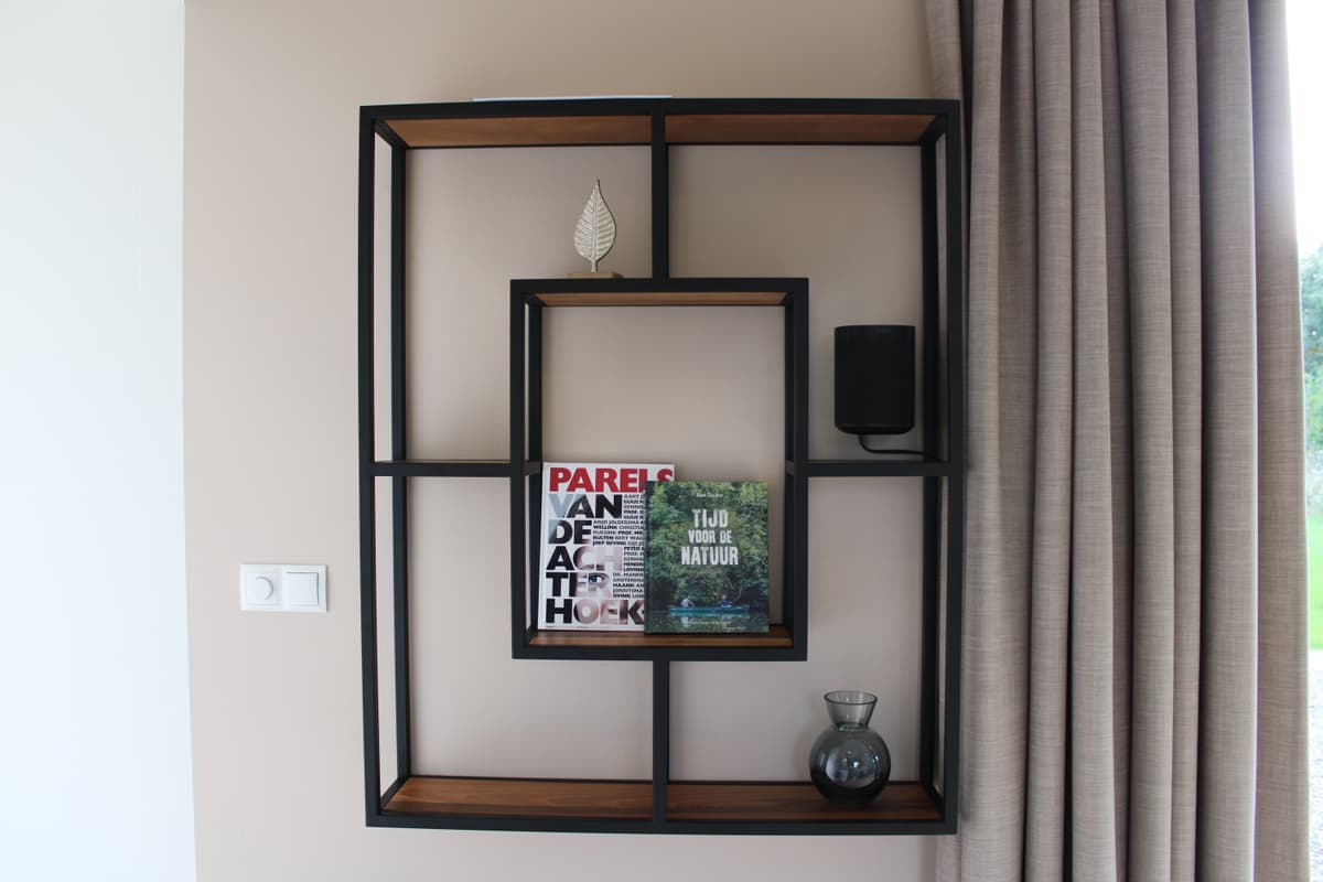 Moderne wandkast met boeken, decoratieve objecten en een vaas, tegen een lichte muur met gordijnen.